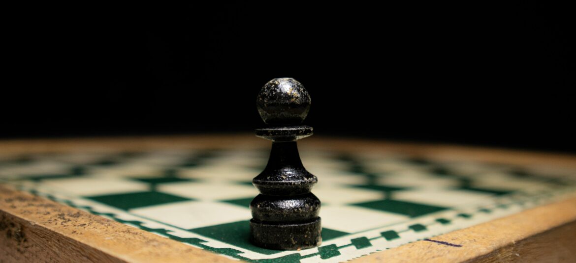 A lone chess pawn positioned at the edge of a wooden chessboard, emphasizing solitude and strategy.